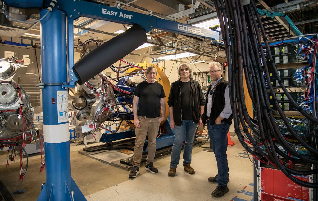 Three men in front of a detector